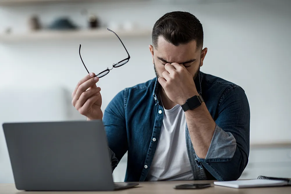 a man sitting at his desk at home and rubbing his irritated, dry eyes
