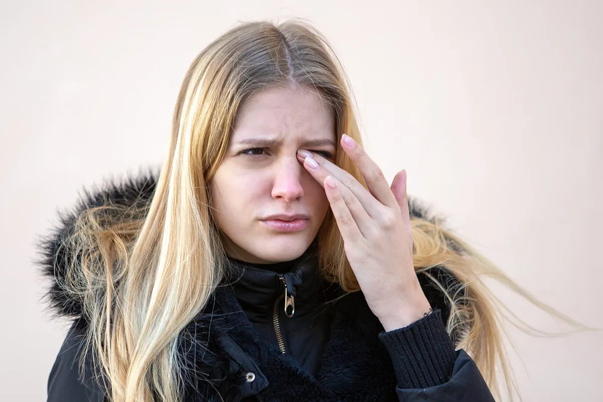 A woman wearing a coat rubs her irritated eyes.