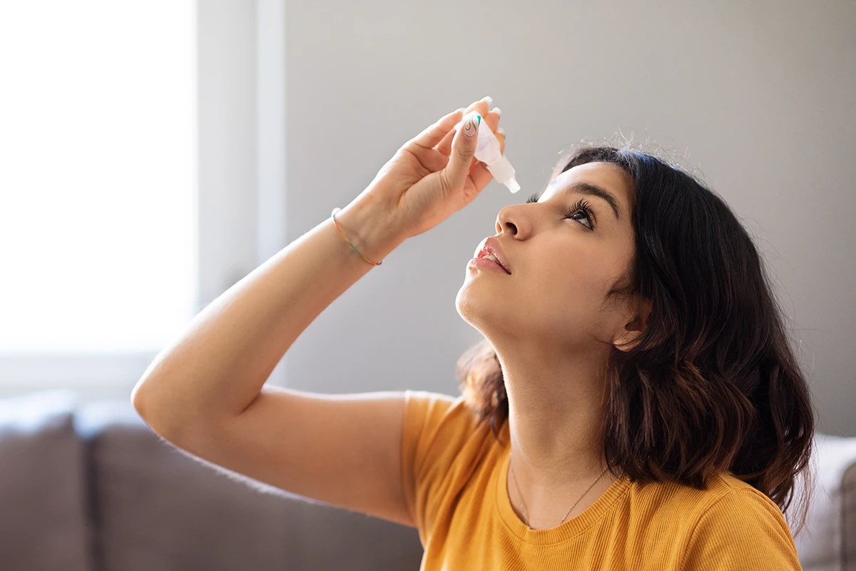 a young woman putting in eye drops for dry eyes at home