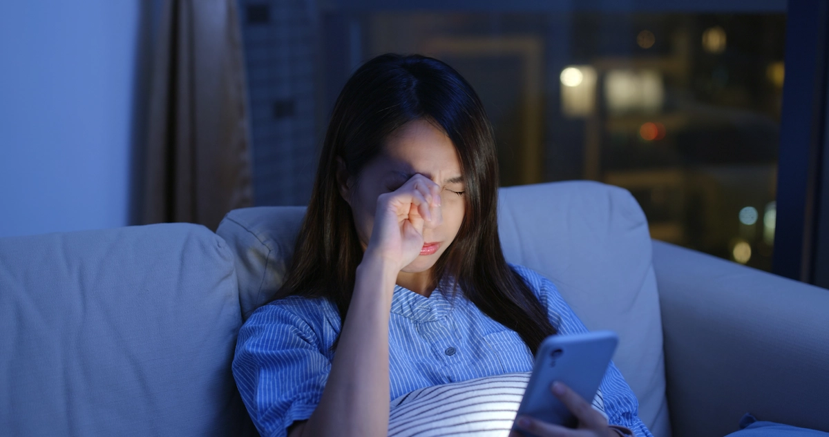 Woman rubbing eye while sitting on couch at night